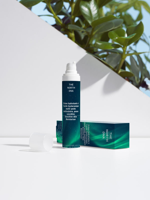 Crème hydratante peaux sensibles The North DNA à l’acide hyaluronique multi-poids moléculaire, flacon pompe et packaging posés sur fond blanc avec décor feuillage naturel, soin apaisant et hydratant anti-rougeurs
